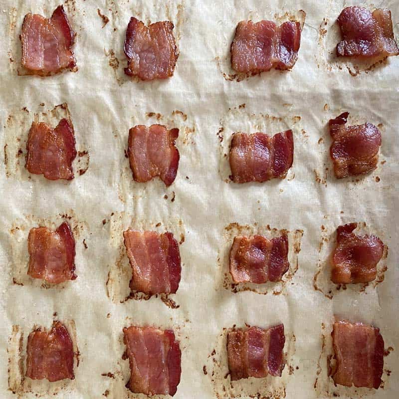 Golden brown crispy bacon squares hot from the oven on a parchment lined baking sheet.