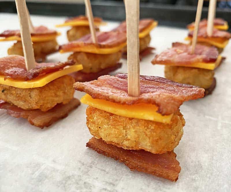 Close up of bacon tater tot cheese appetizers on skewers arranged on a parchment lined baking sheet